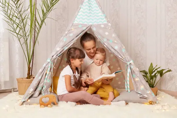 Une maman qui fait la lecture pour  ses 2 filles dans un lit tipi Montessori