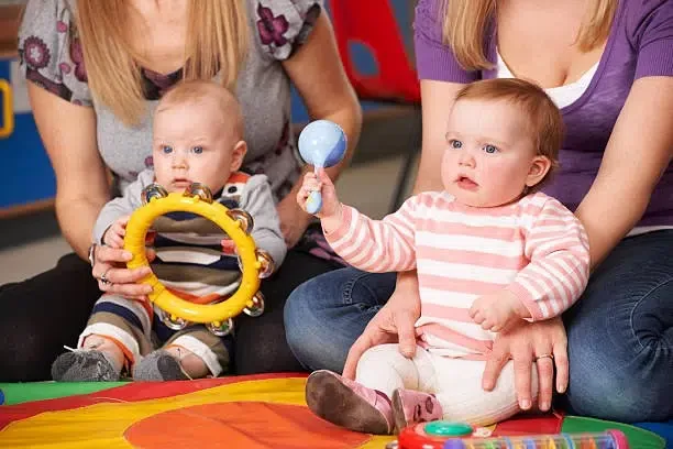 Deux bébés avec ses mamans jouant à des hochets sur un tapis de motricité