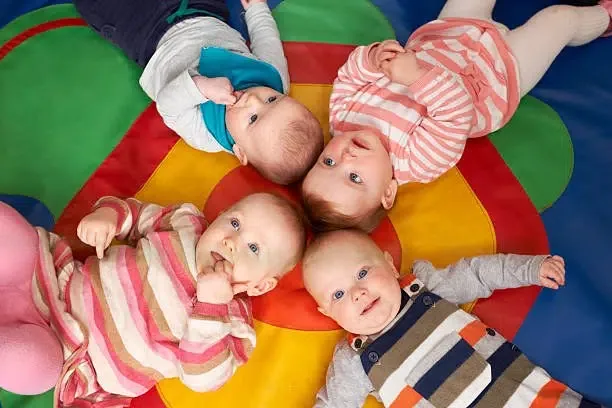 4 bébés allongés sur un tapis de motricité