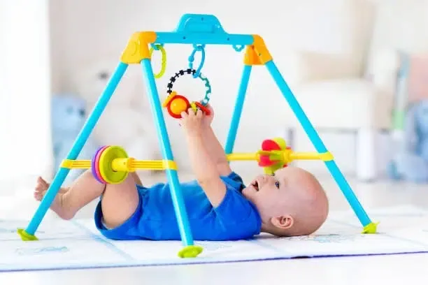 Un bébé sur un tapis de motricité équipé d'un jouet suspendu